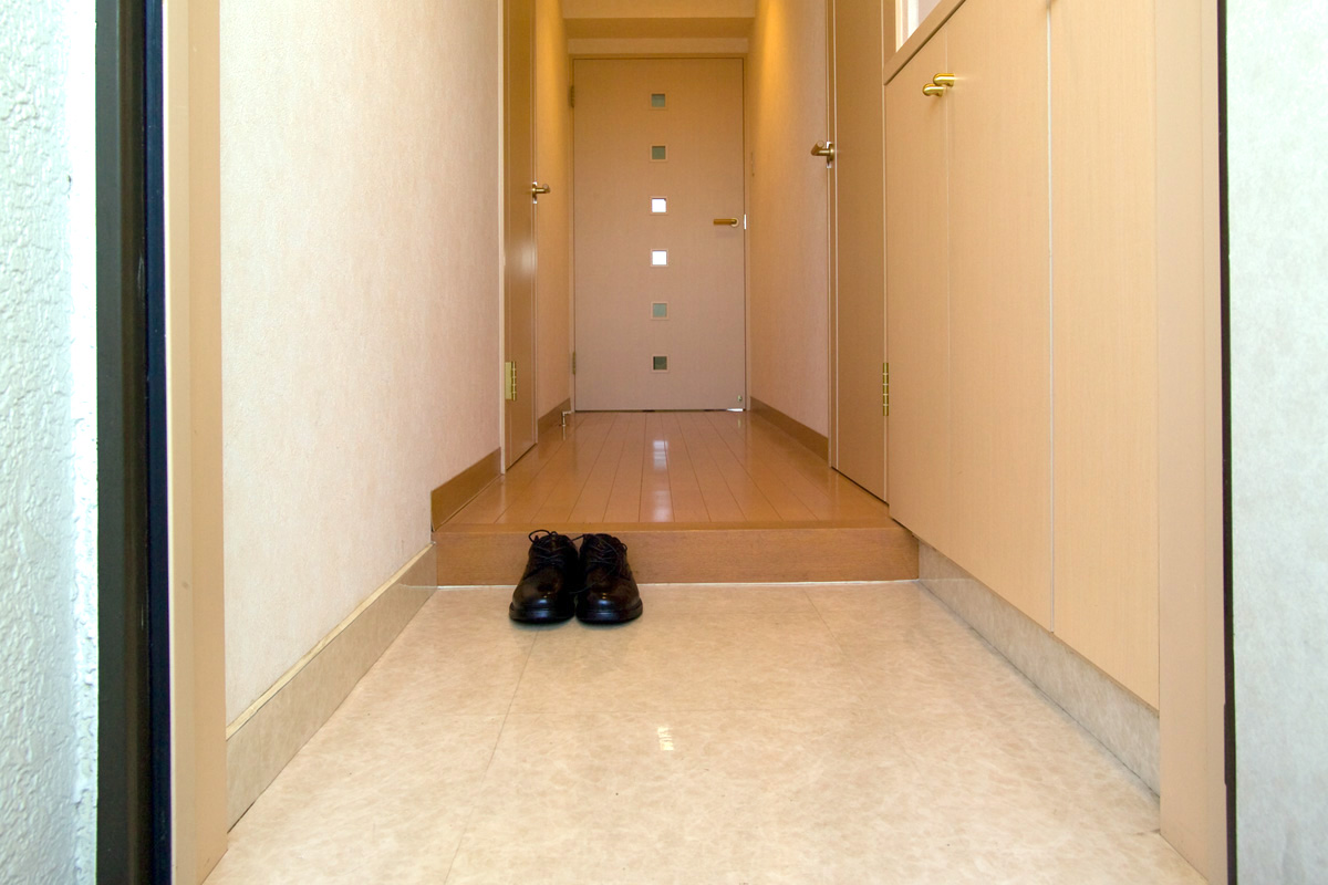 Narrow residential entrance with shoes kept at the threshold and a clear hallway beyond