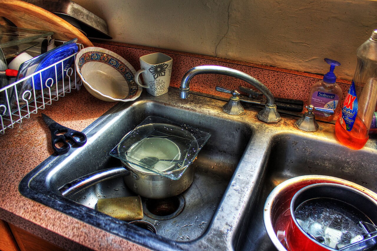 Kitchen sink filled with dishes, with different container shapes waiting to be cleaned